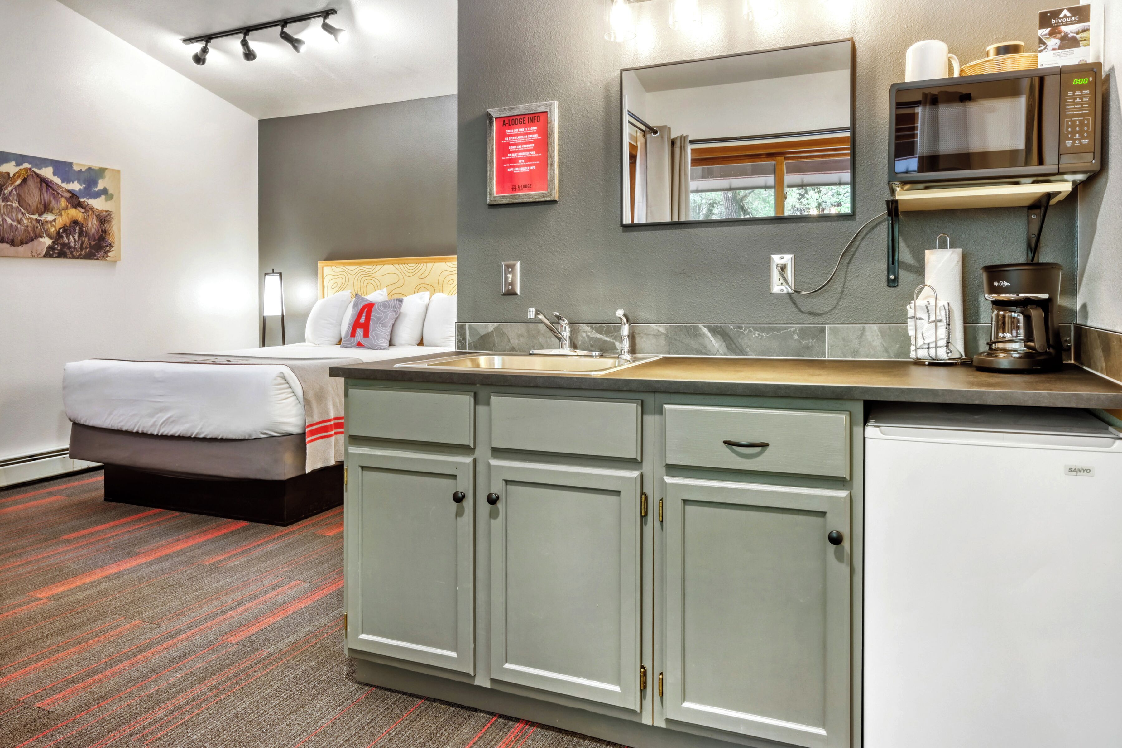 A hotel room with a bed, a sink, a microwave, a coffee maker, and a cabinet.