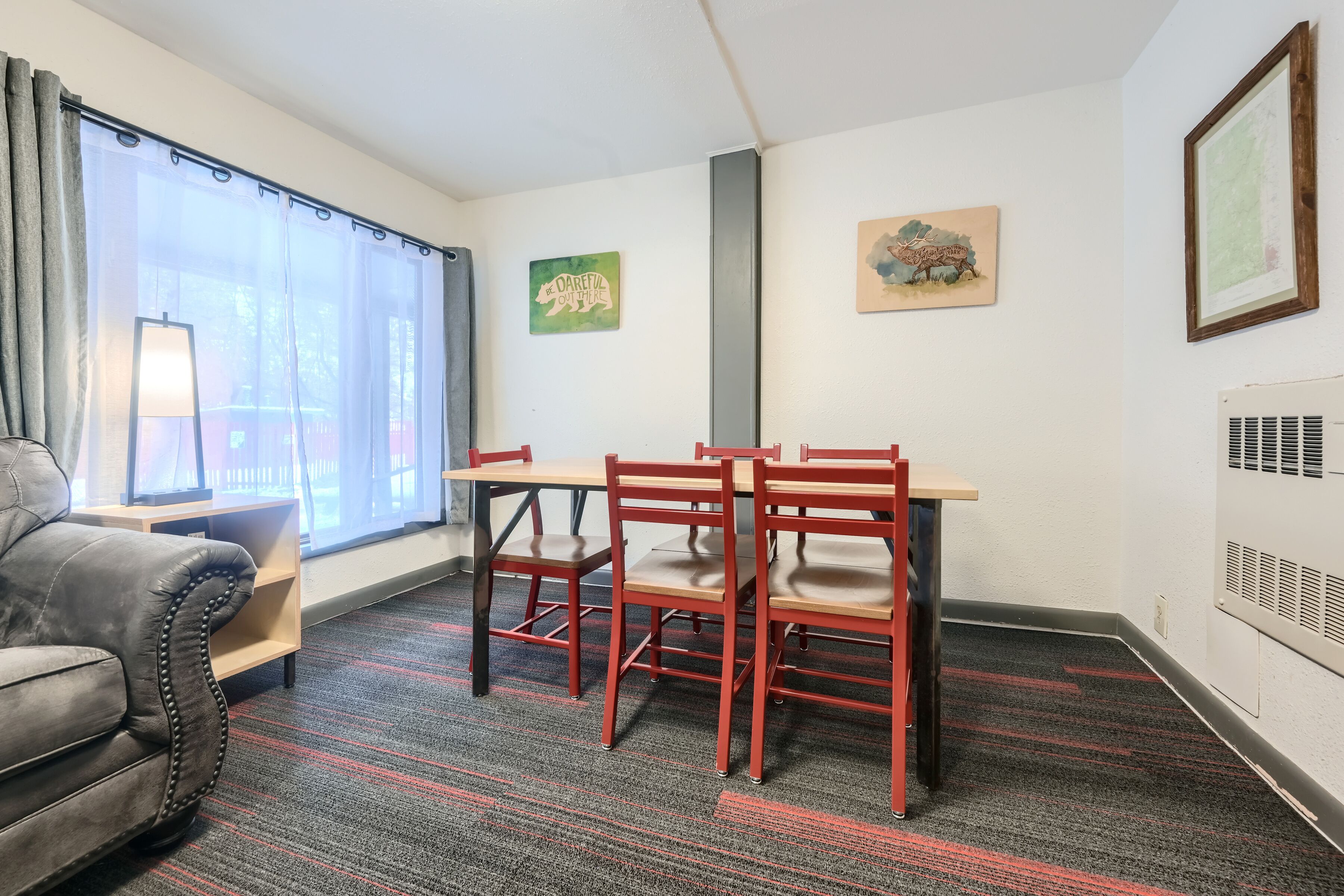 A room with a desk, two chairs, a sofa, and a window with curtains.