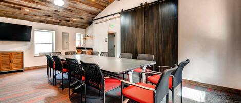 Una sala de conferencias con una gran mesa, sillas rojas y negras, techo de madera y una puerta corrediza.