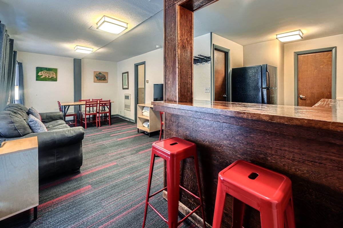 Un salon moderne avec un canapé, des tabourets rouges, un comptoir de bar en bois et un coin repas comprenant des chaises et une table.