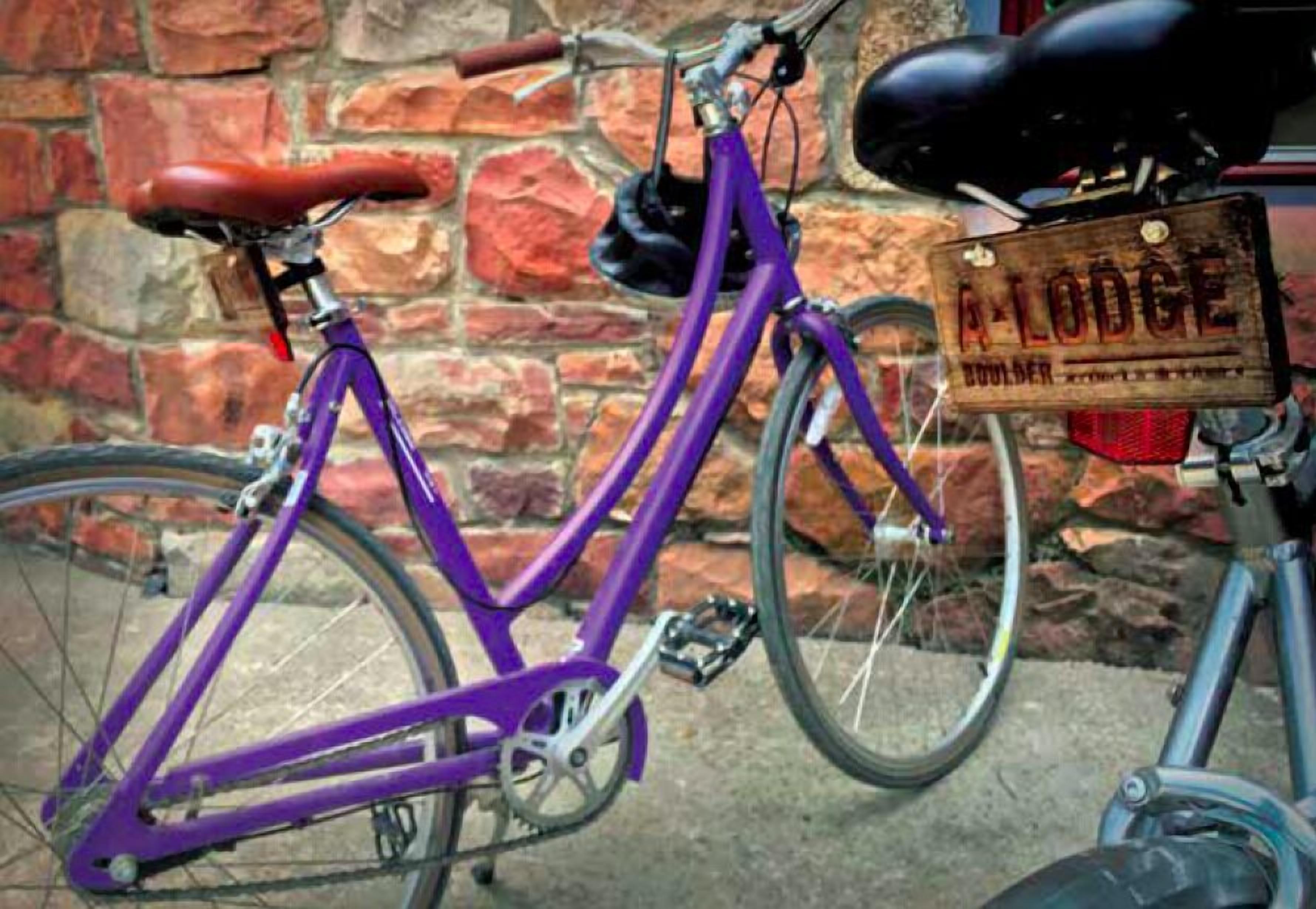 Una bicicleta púrpura con un letrero de madera que dice 'A LODGE' sujeto a una pared de ladrillo.