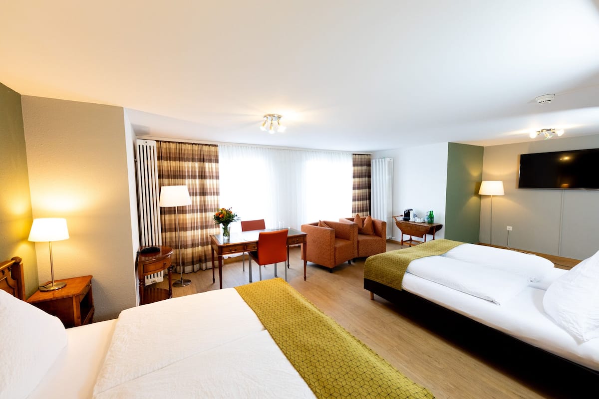 A hotel room with two beds, a desk, a chair, a TV, and a window with curtains.