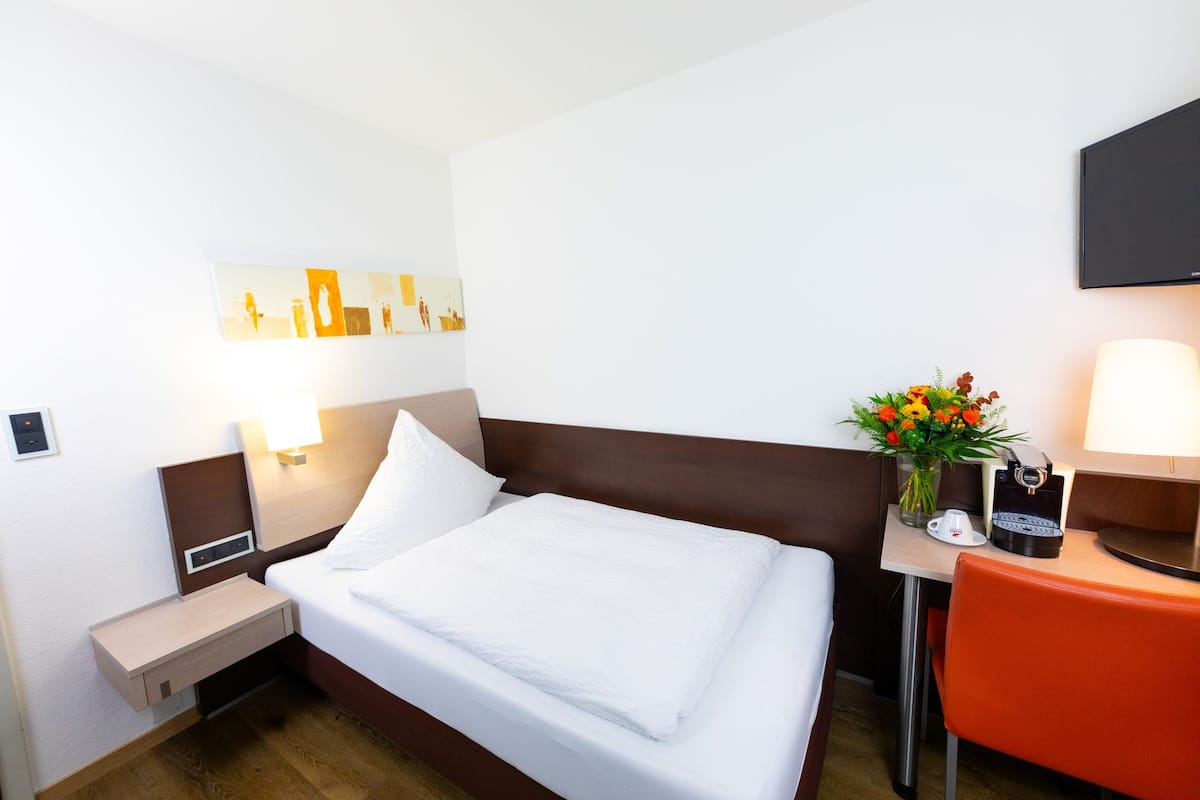 A hotel room with a bed, bedside table, lamp, chair, and a wall-mounted TV.