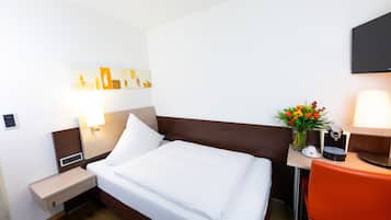 A hotel room with a bed, bedside table, lamp, chair, and a wall-mounted TV.