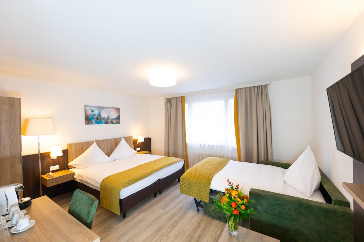 A hotel room with a bed, a desk, a chair, a lamp, a painting, and a vase with flowers.