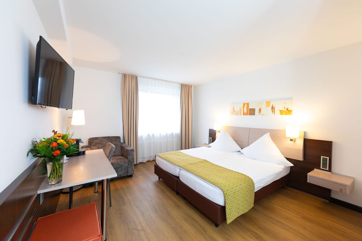 A hotel room with a bed, a desk, a chair, a TV, and a window with curtains.