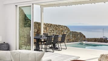 Un área de comedor al aire libre moderna con piscina, muro de piedra y vista al océano.