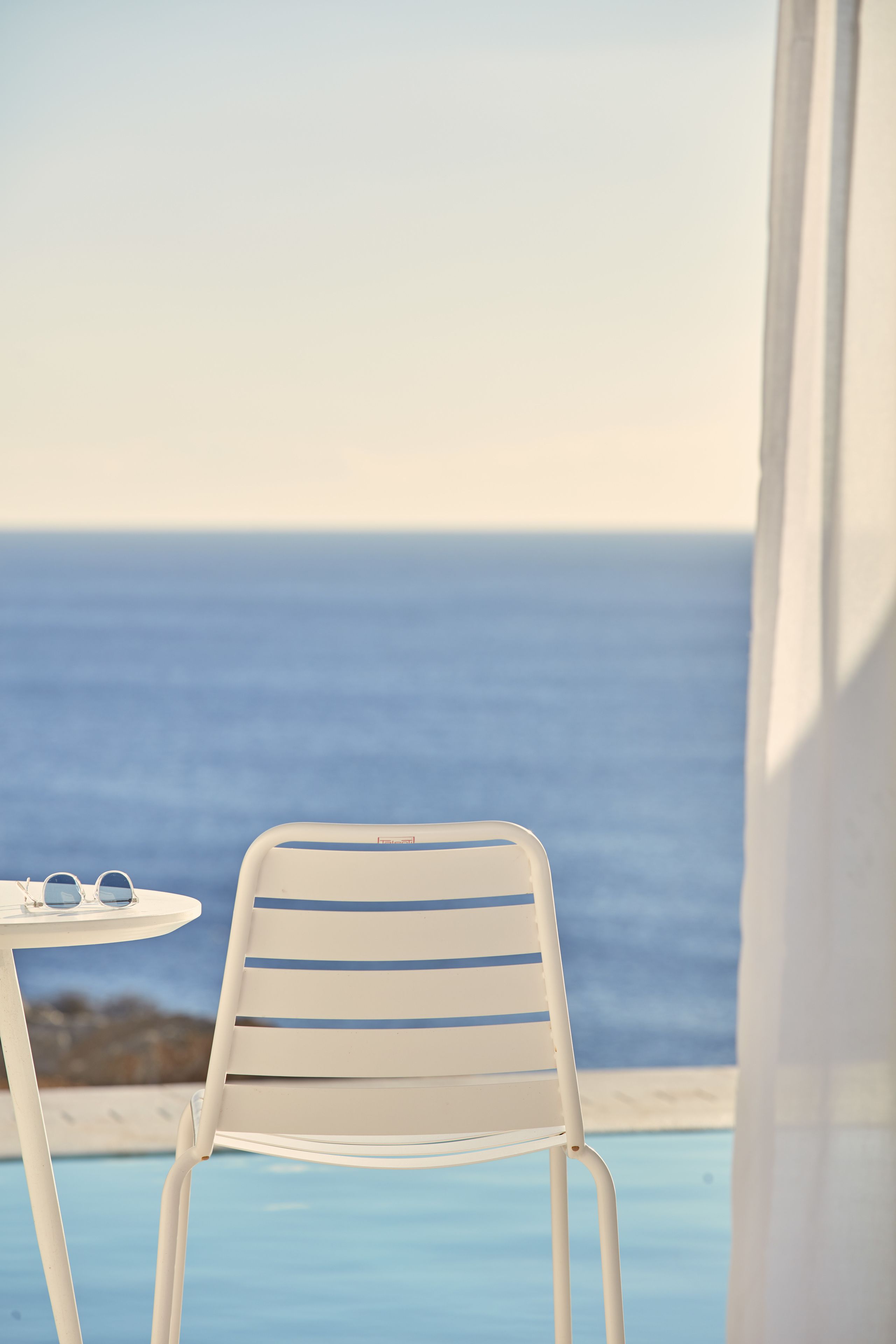 A white metal chair and table by a pool with a view of the ocean.