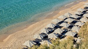 A beach with rows of umbrellas and lounge chairs, indicating a resort setting. - Royal Myconian - Leading Hotels of the World (Mykonos)