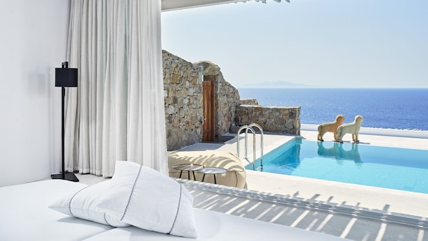 A modern bedroom with a large bed, a view of the sea, and a pool with two decorative dogs. - Royal Myconian - Leading Hotels of the World (Mykonos)