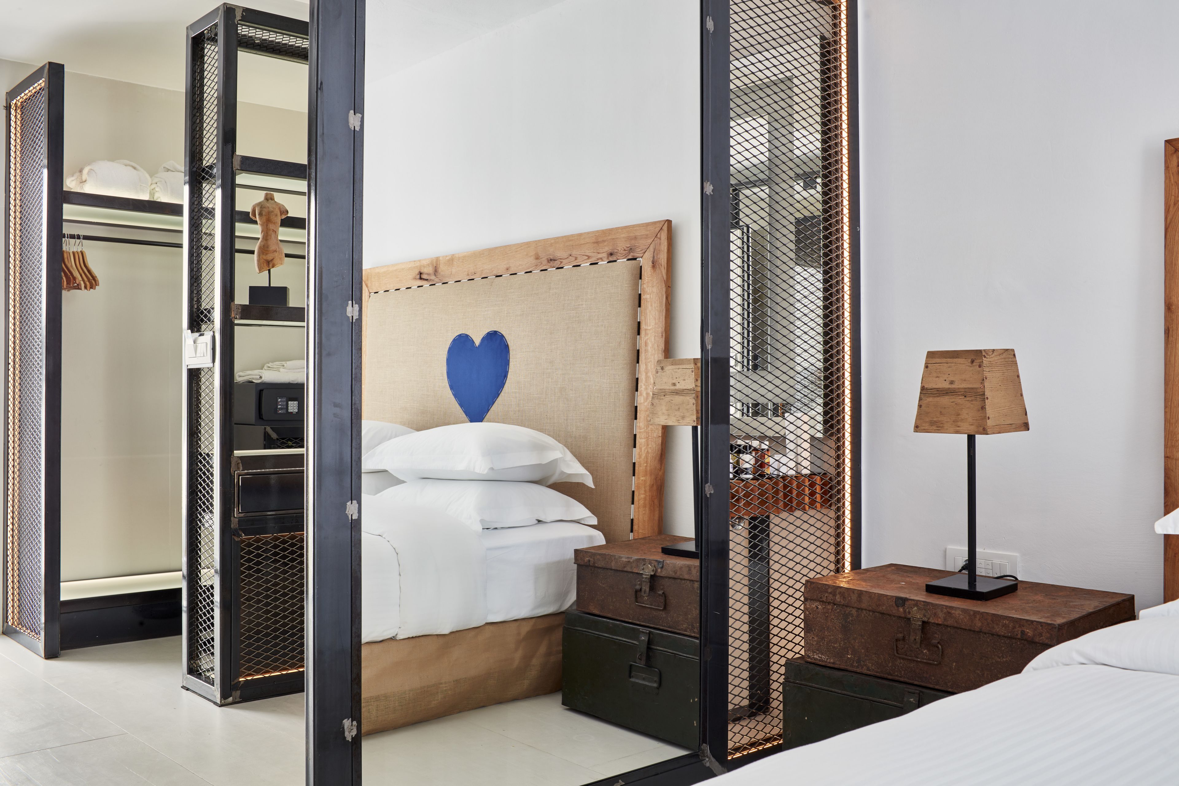 A hotel room with a bed, a nightstand with a lamp, a dresser, and a wardrobe with a mirror.