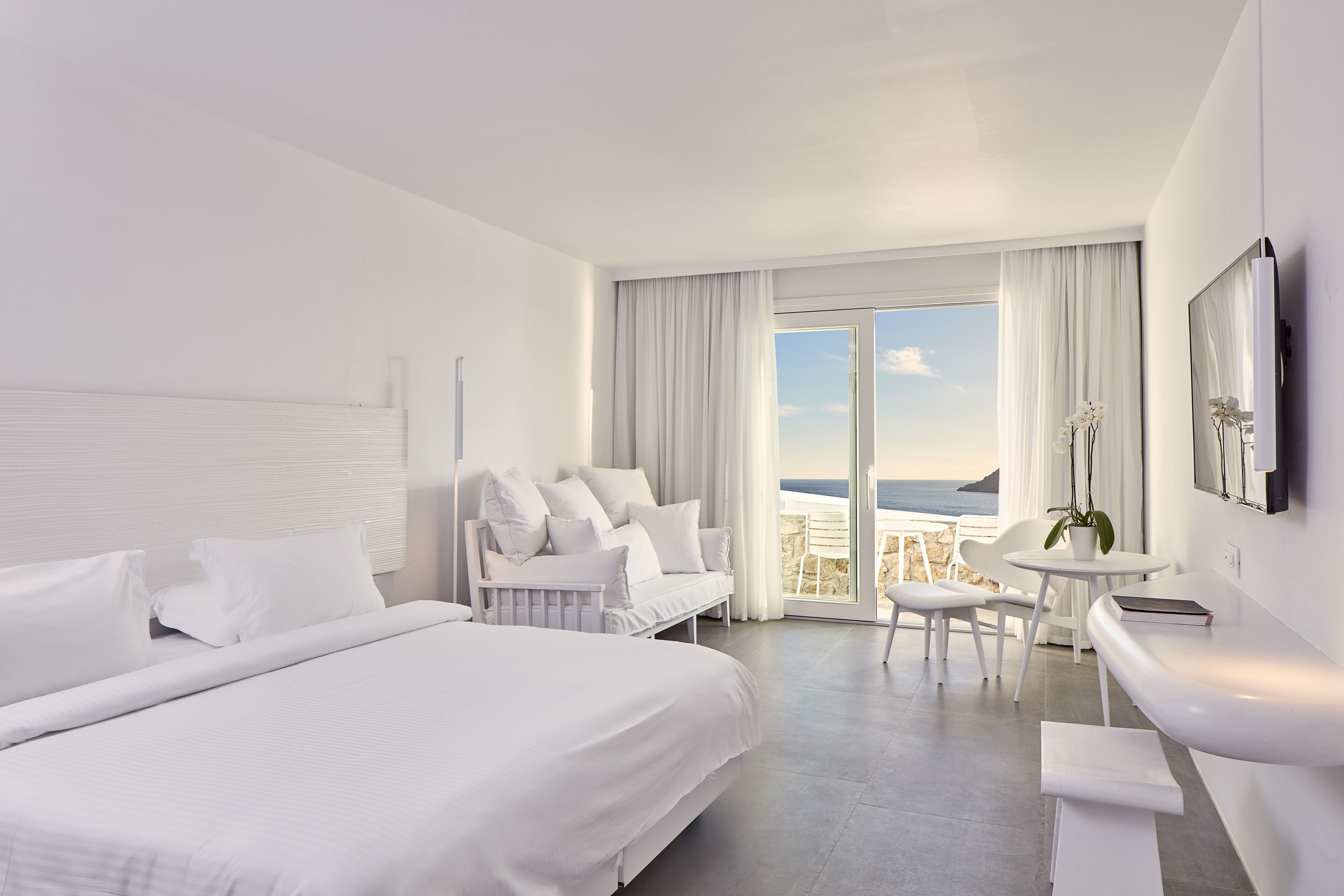 Quarto de hotel moderno com uma cama grande, um sofá, área de jantar e vista para o oceano.