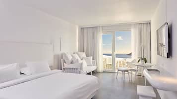Quarto de hotel moderno com uma cama grande, um sofá, área de jantar e vista para o oceano.