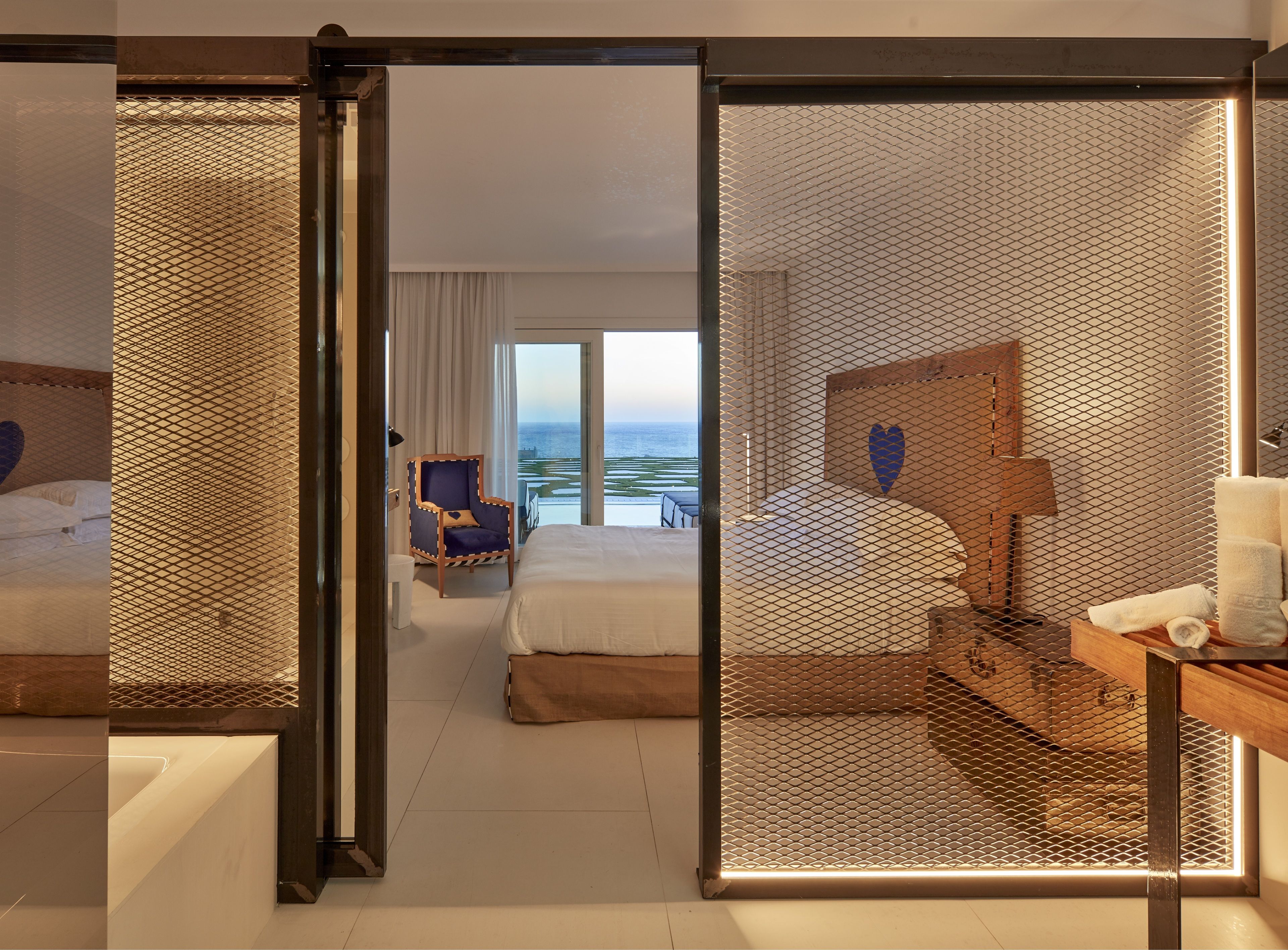 Ein Hotelzimmer mit zwei Betten, einem Sessel, einem Schreibtisch und Meerblick.