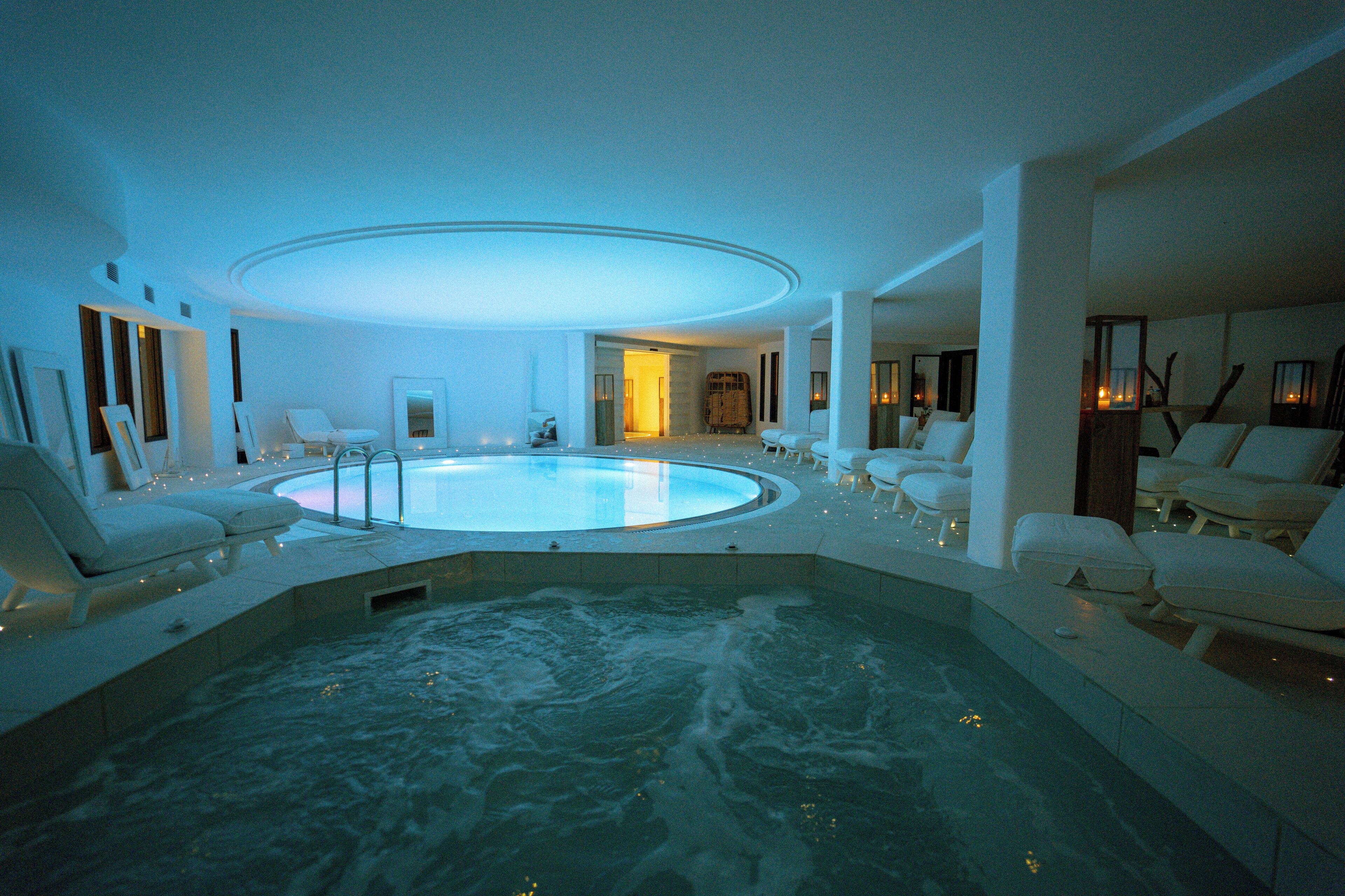 A large indoor swimming pool with lounge chairs and a circular ceiling design.