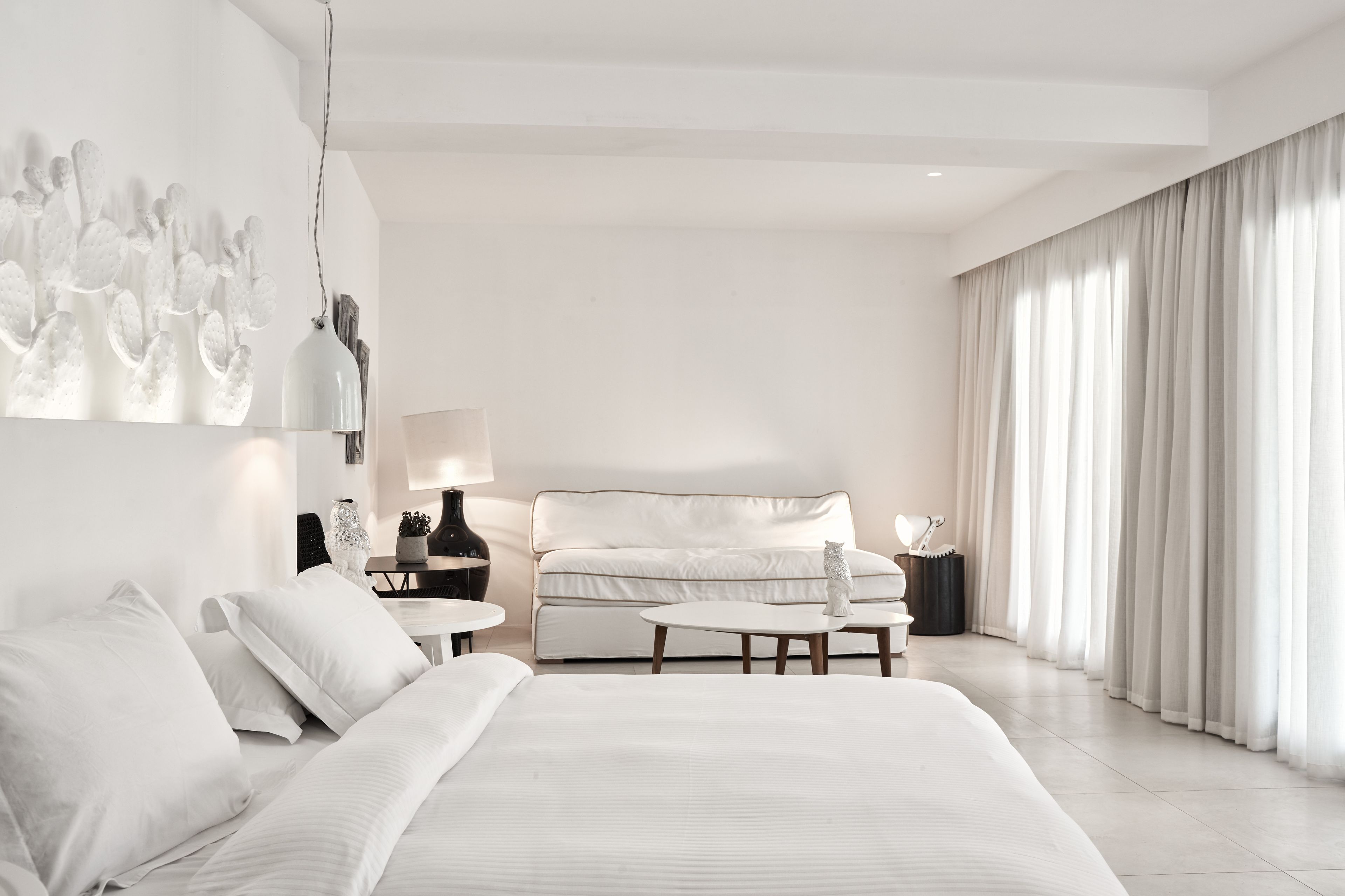 A modern hotel room with a large bed, a sofa, a small table, and a lamp.