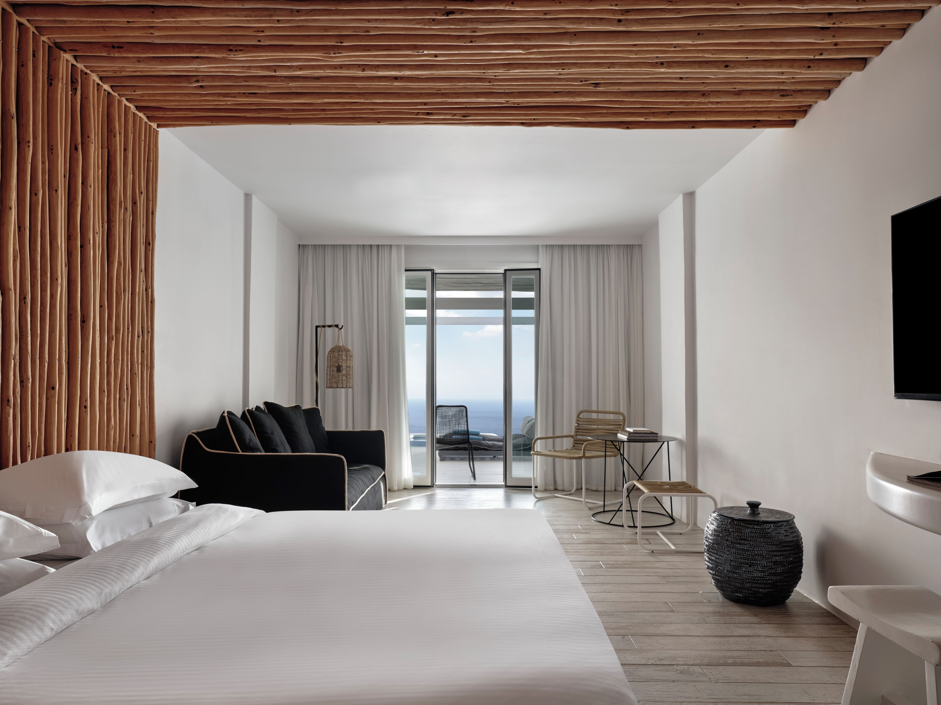 Une chambre d’hôtel moderne dotée d’un grand lit, d’un coin salon avec une table et des chaises, d’une télévision et offrant une vue sur l’extérieur.