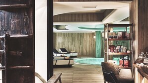 Un interior moderno con suelo de madera, una piscina, una zona de estar con sofá y sillones, y un bar con estantes llenos de botellas.