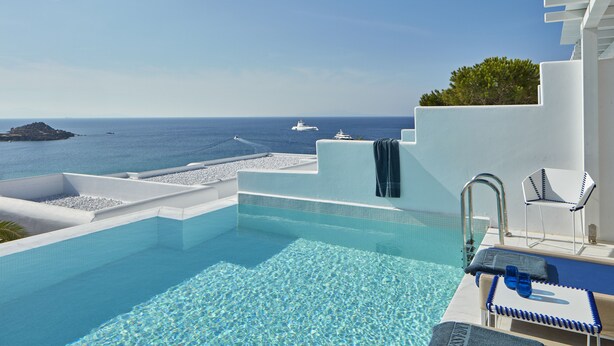 Ein Pool ohne erkennaren Rand mit klarem, blauem Wasser, einer weißen Kante und Blick auf das Meer mit Booten.