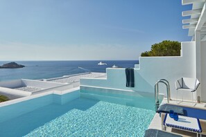Une piscine à débordement à l’eau d’un bleu cristallin, avec un bord blanc et une vue sur la mer, où l’on peut apercevoir des bateaux.