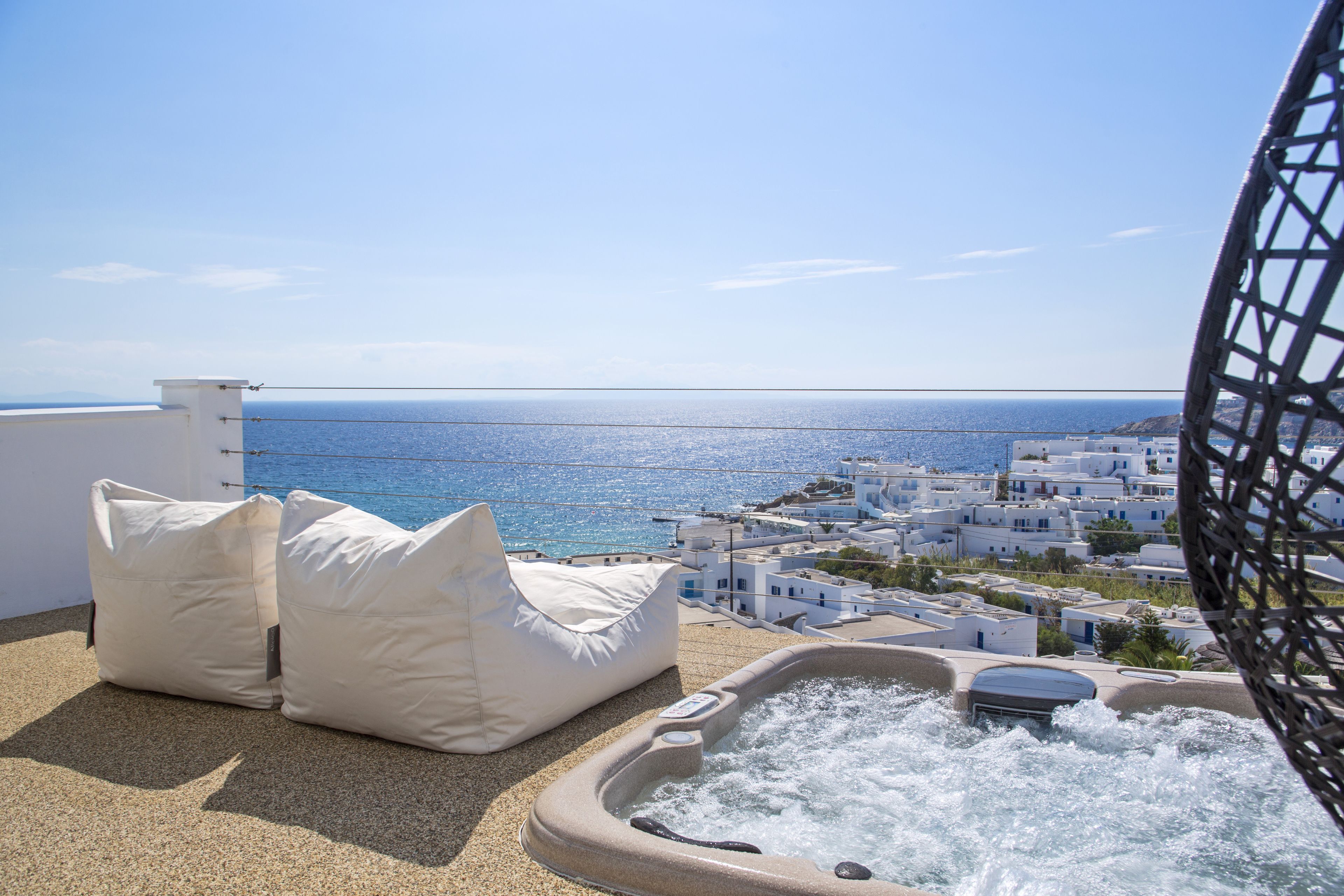 A balcony with a hot tub, white cushions, and a view of the sea and white buildings.