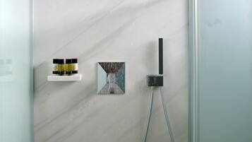 Une douche moderne dotée d’un pommeau de douche à pluie, d’un pommeau de douche à main et d’une petite étagère pour les articles de toilette.