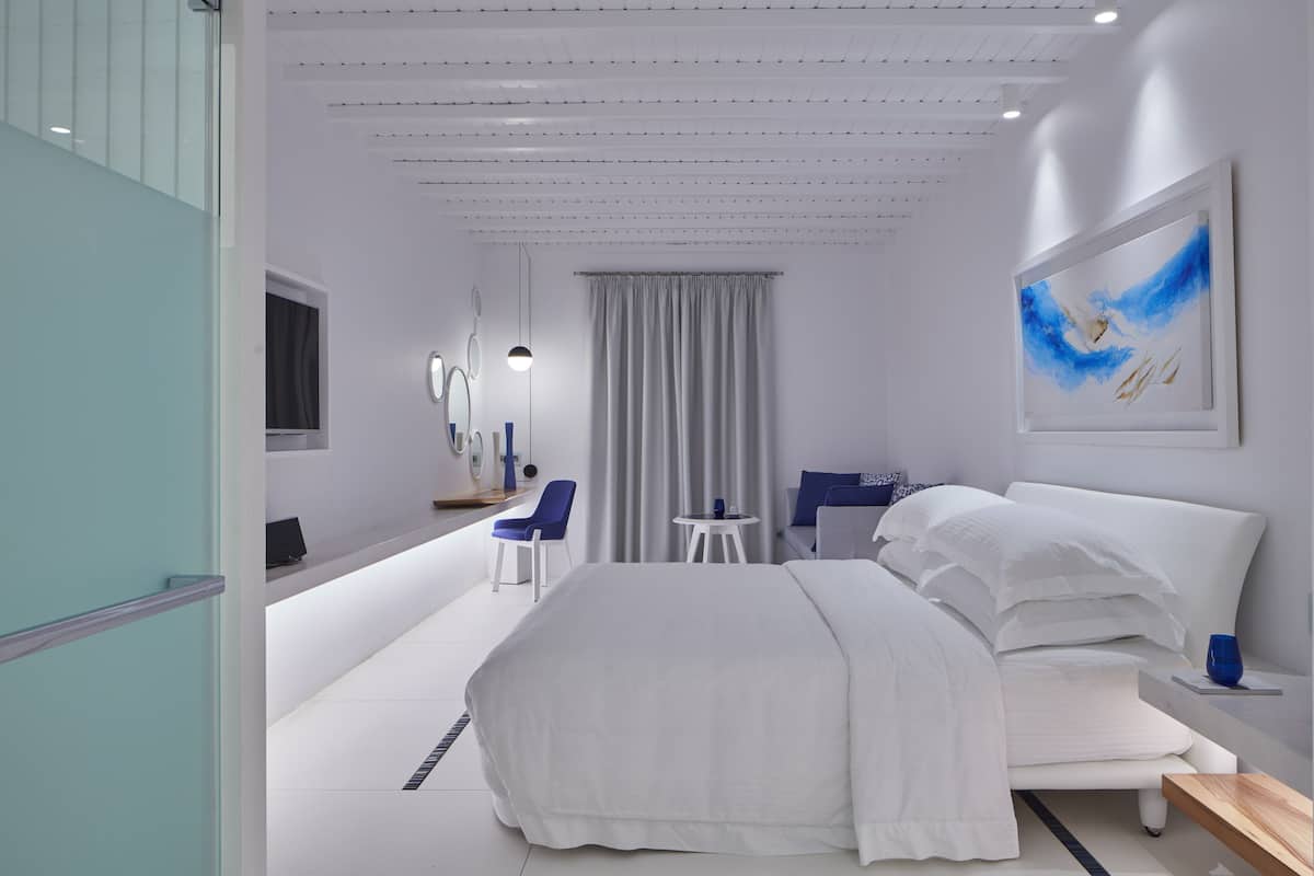 Een moderne hotelkamer met een groot bed, een bureau met stoel, een klein tafeltje en een schilderij aan de muur.