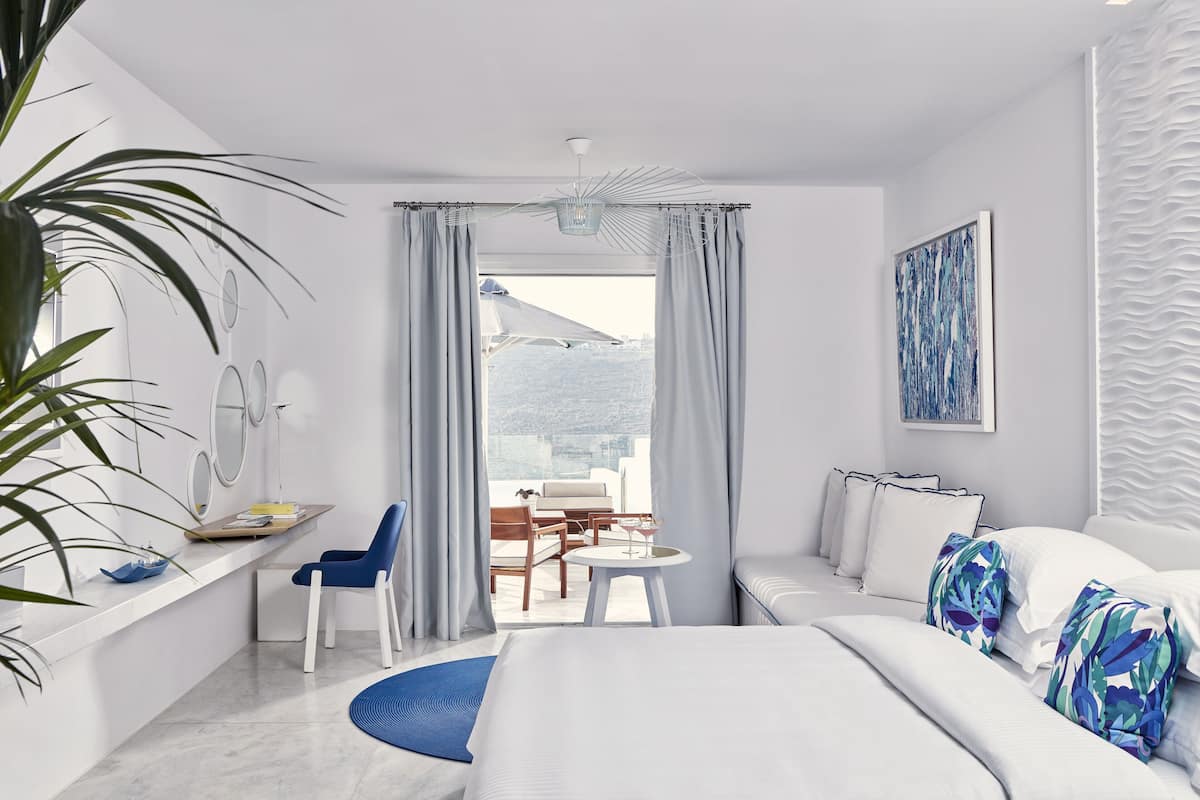 Een moderne hotelkamer met een bed, een bureau, een stoel, een klein tafeltje en uitzicht op de omgeving.