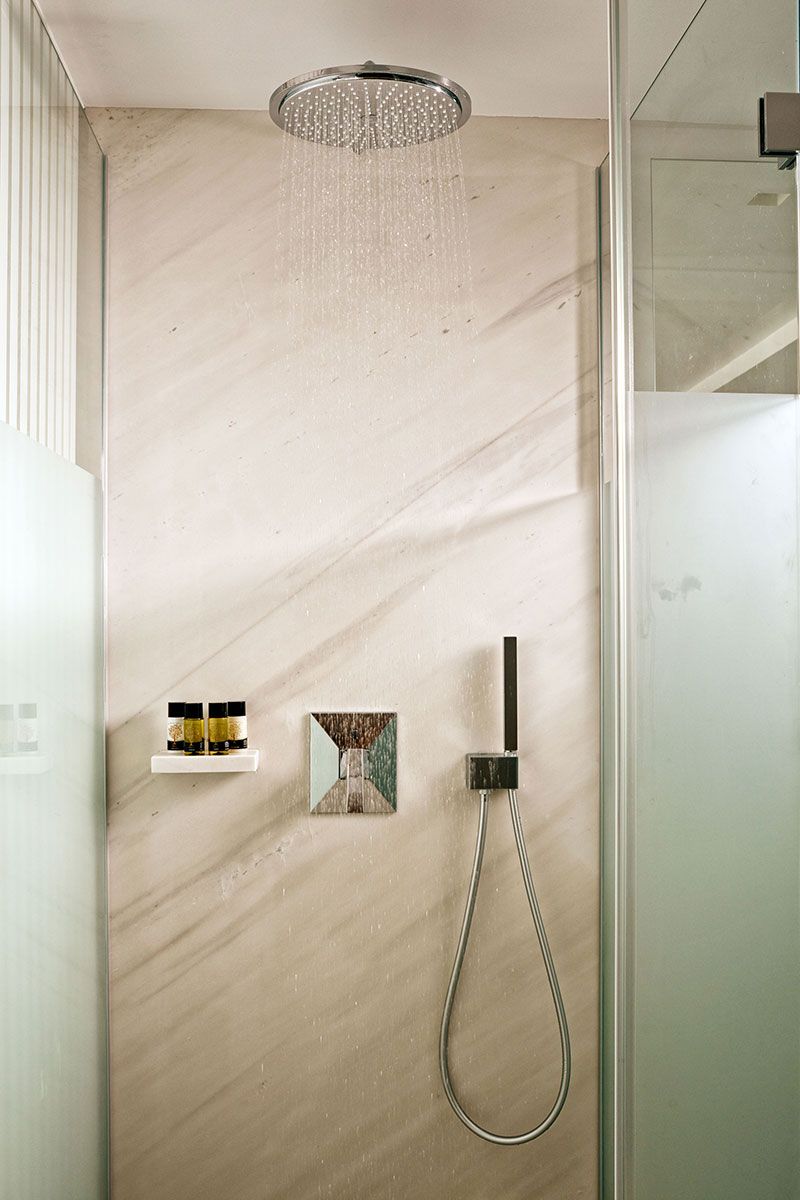 Eine Dusche mit Regendusche, Handbrause und Seifenspender an einer Marmorwand.