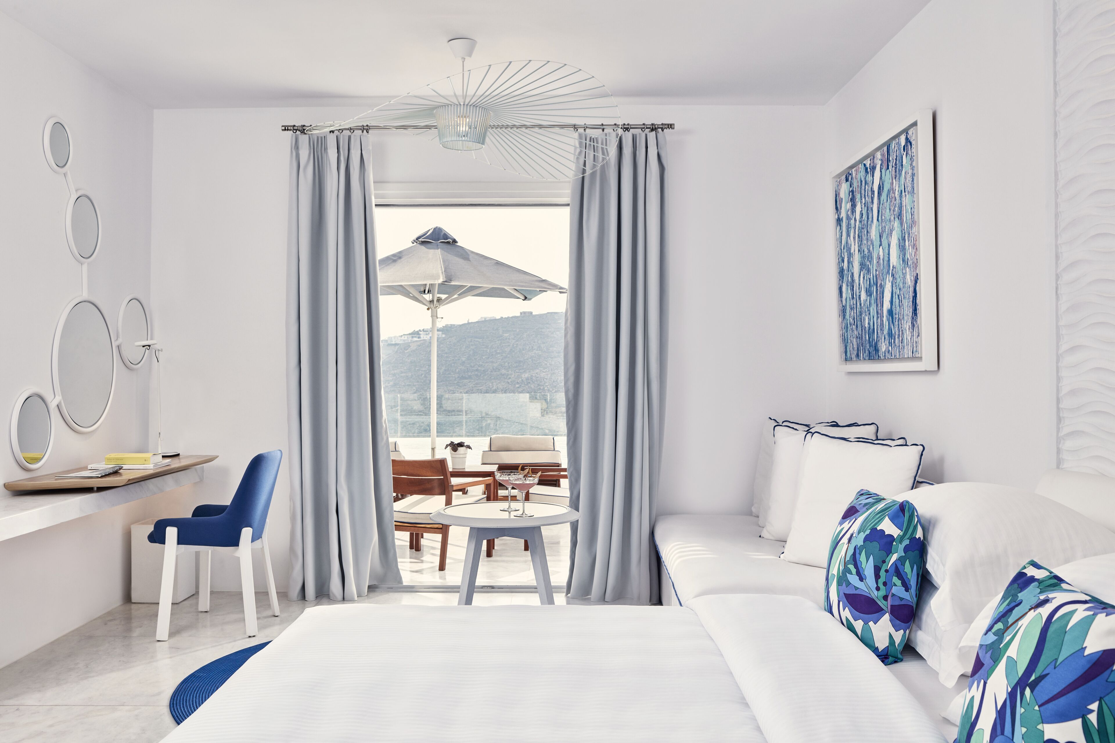 Una habitación de hotel moderna con cama, escritorio, silla, mesa redonda y balcón con sombrilla.
