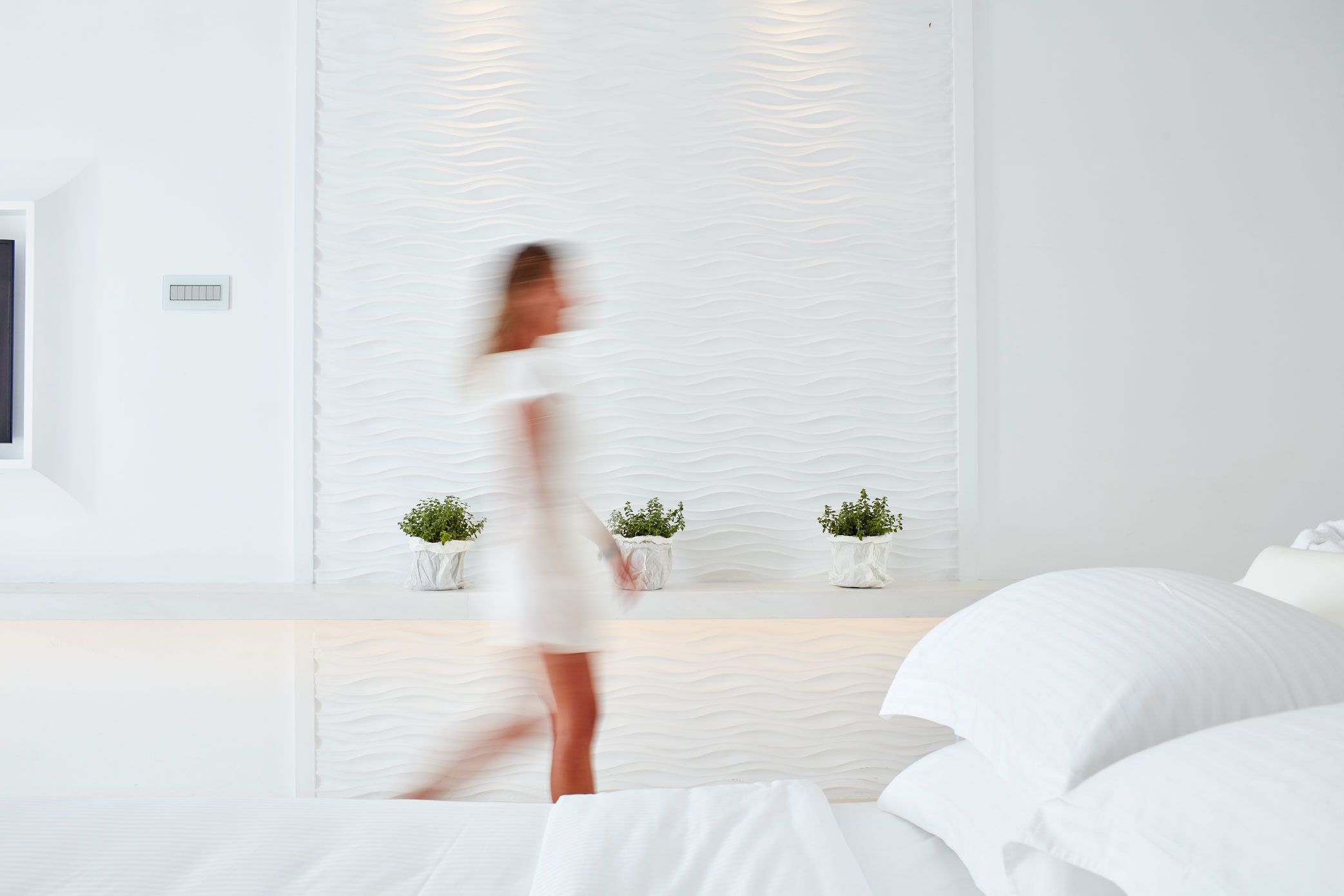 Un dormitorio moderno con una cama, una mesita de noche con dos plantas en macetas y una pared con textura.