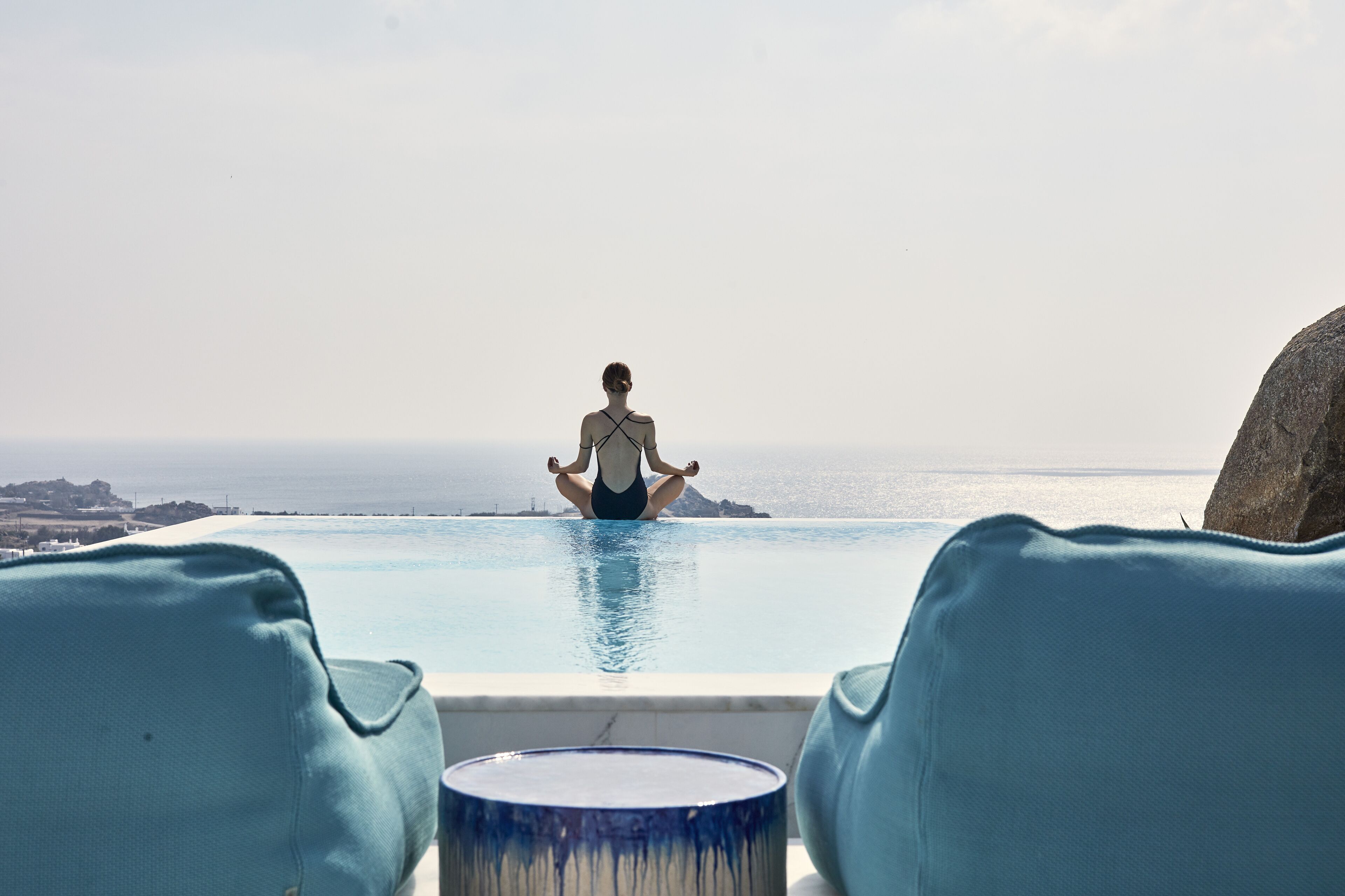 A person meditating in a pool with a view of the sea and distant land.