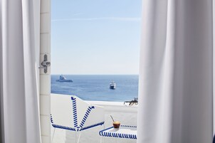 Vista de varanda com guarda branco, mesa com bebida e um navio ao longe.
