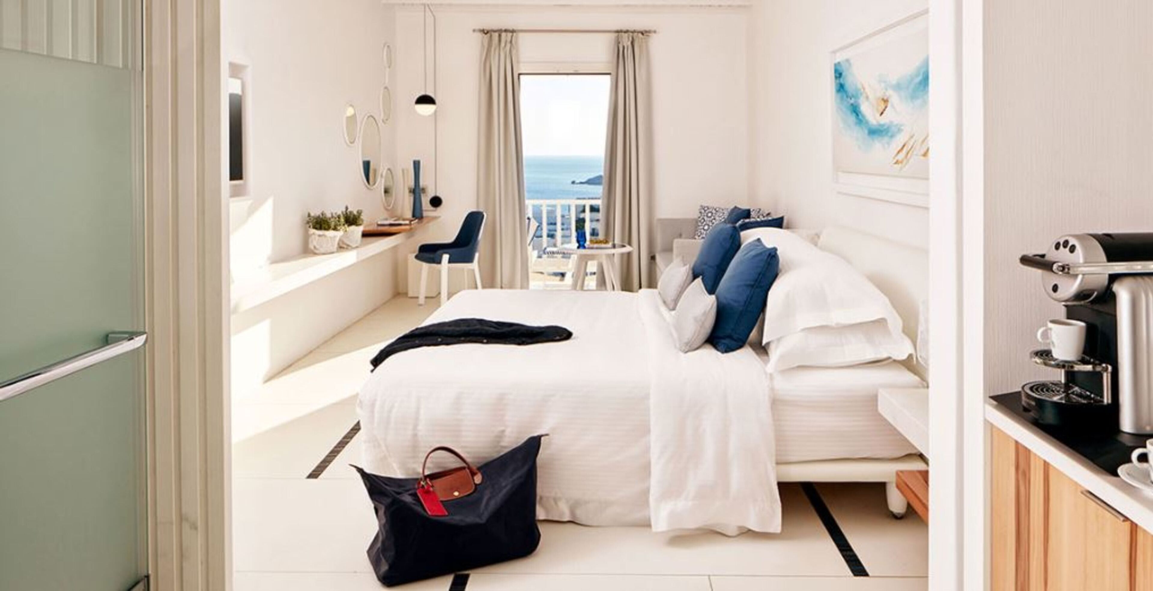 Une chambre d’hôtel équipée d’un lit, d’un bureau, d’une chaise, d’une machine à café et offrant une vue sur la mer.