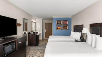 A hotel room with a large bed, a TV, a desk with a microwave, and a bathroom visible in the background.