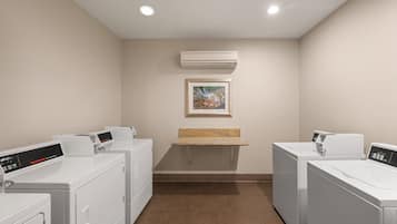 Un cuarto de lavandería con dos lavadoras, una secadora, un estante pequeño y un equipo de aire acondicionado.