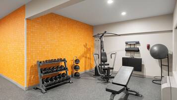 Un gimnasio con equipo de ejercicio, una banca y una pared con diseño decorativo.