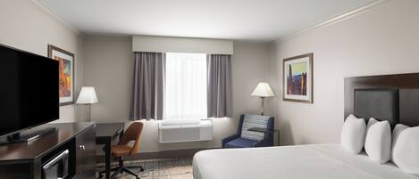 A hotel room with a bed, a desk with a television, a chair, two lamps, and a window with curtains.