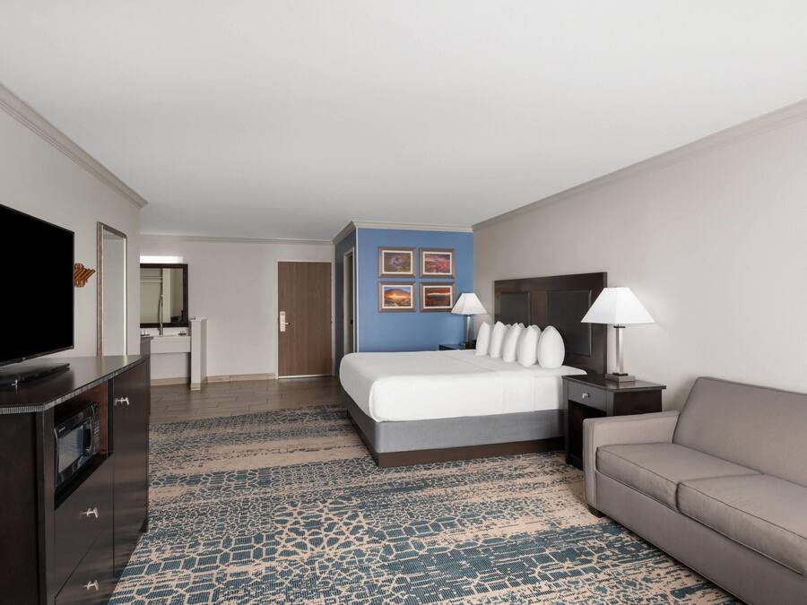 A hotel room with a bed, a TV, a sofa, a desk, and a lamp.