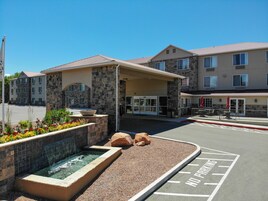 A hotel entrance with a covered walkway, a small water feature, and a parking area marked for handicapped parking.