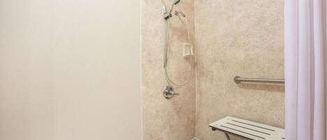 A shower area with a handheld showerhead, a wall-mounted faucet, and a grab bar.