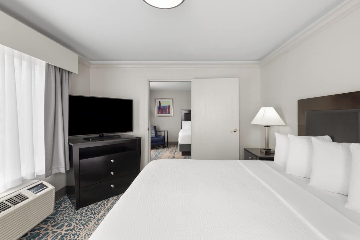 Et hotelværelse med en stor seng, et fladskærms-tv, et skrivebord med en lampe og en stol.