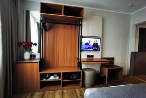 A modern hotel room with a wooden entertainment unit, a television, a small table, and a bed. - Hotel Italia (Munich)
