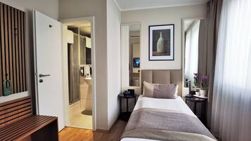 A hotel room with a bed, bedside tables, a mirror, a painting, and a wooden bench.