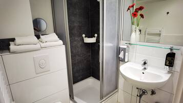 A modern bathroom with a glass shower enclosure, a white sink with a hand wash station, and a mirror above the sink.