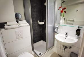 Un baño moderno con cabina de ducha de vidrio, un lavamanos blanco con estación de lavado y un espejo sobre el lavamanos.