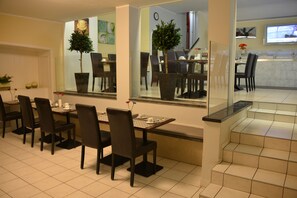 A dining area with a long table, multiple chairs, and potted plants. - Hotel Italia (Munich)