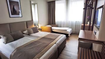 Quarto de hotel com uma cama grande, uma cama menor, uma escrivaninha e uma televisão.