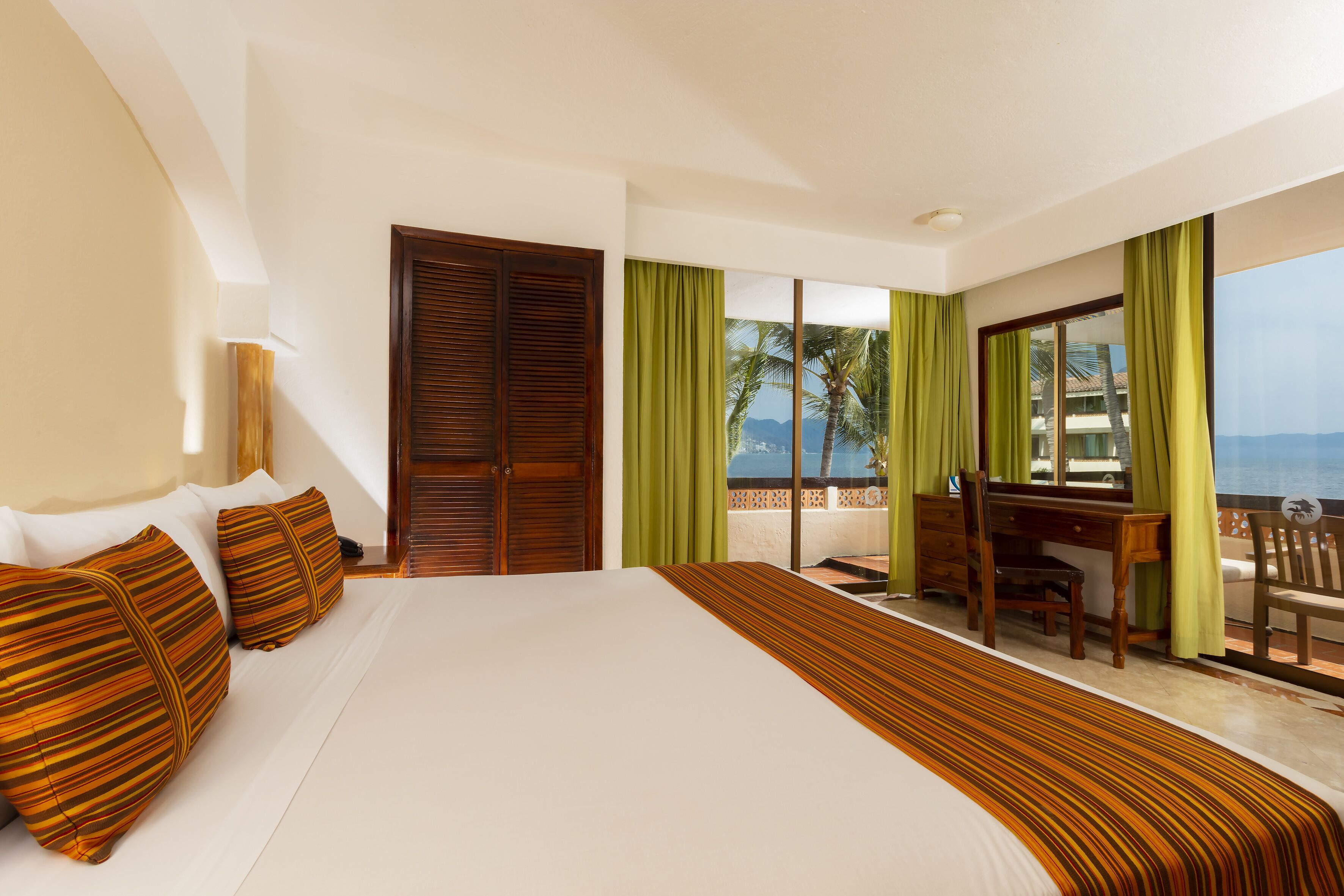 A hotel room with a large bed, a desk, and a view of the sea.