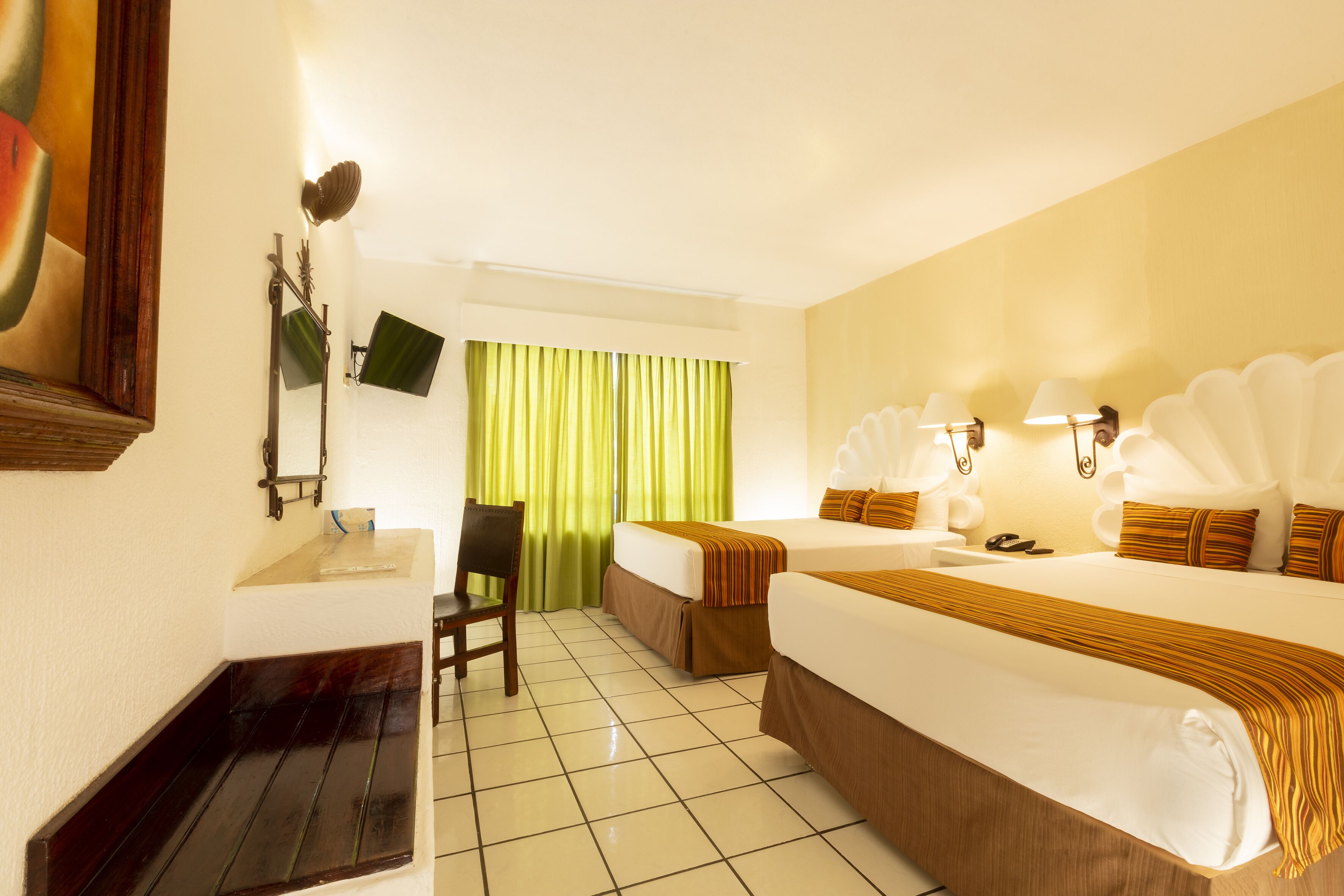 A hotel room with a bed, a desk, a chair, a TV, and a window with curtains.